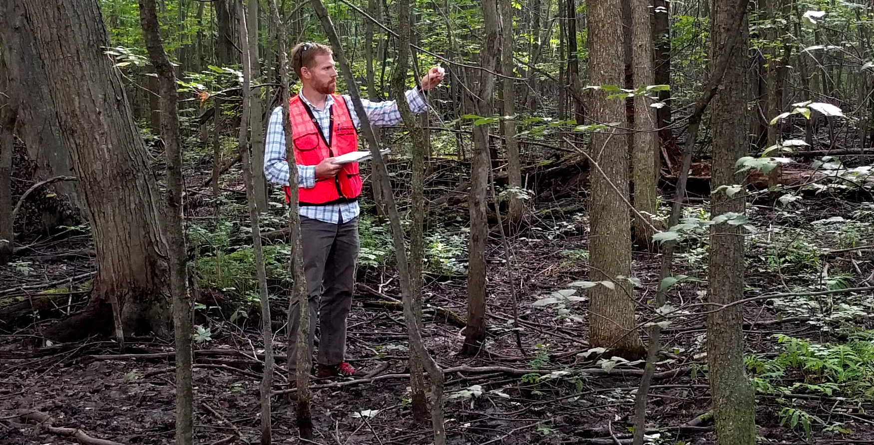 Jordan Marshall standing in a forest collecting basal area data
